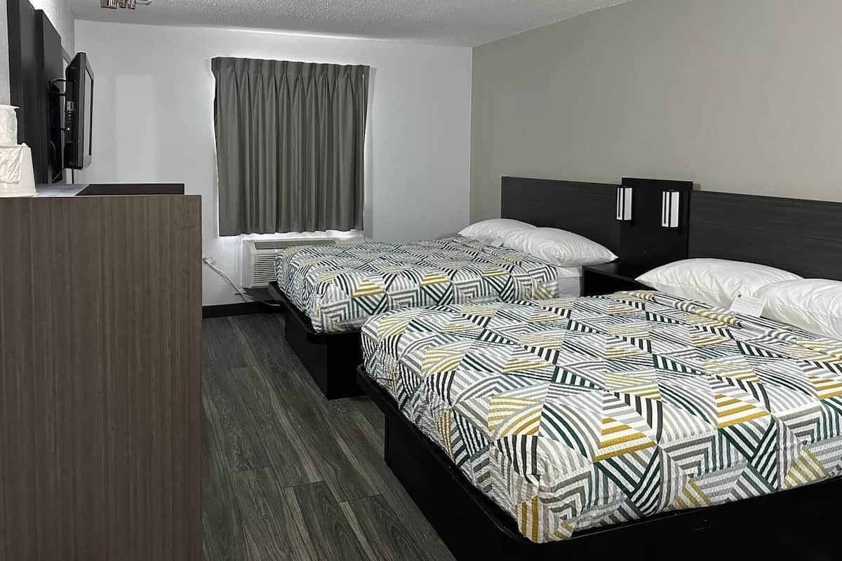 A hotel room with two beds, a desk, a television, and a window with curtains.