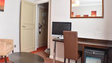 A hotel room with a desk, chair, computer, and a small refrigerator.