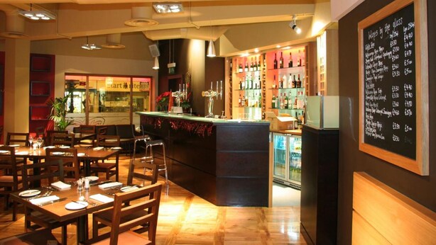 Um restaurante com área de bar, mesas e cadeiras de madeira.