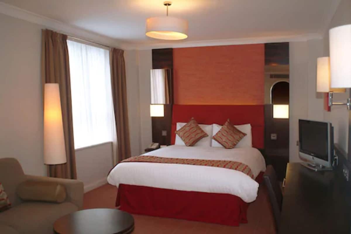 A hotel room with a large bed, a TV, a desk, and a chair.