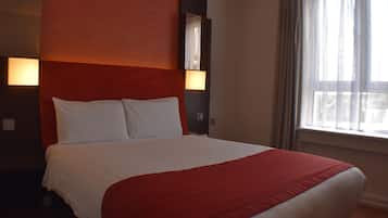 Ein Hotelzimmer mit einem großen Bett, einem roten Kopfteil, zwei Nachttischlampen und einem Fenster mit Vorhängen.