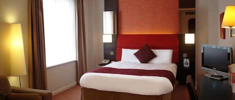 A hotel room with a large bed, a desk, a chair, a TV, and a window with curtains.