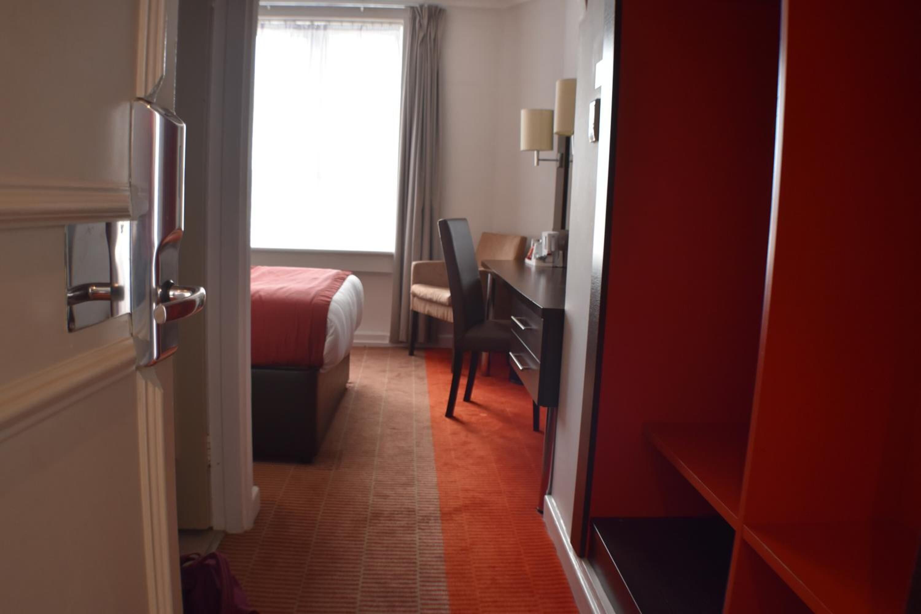 Ein Hotelzimmer mit Bett, Schreibtisch, Stuhl und einem Fenster mit Vorhängen.