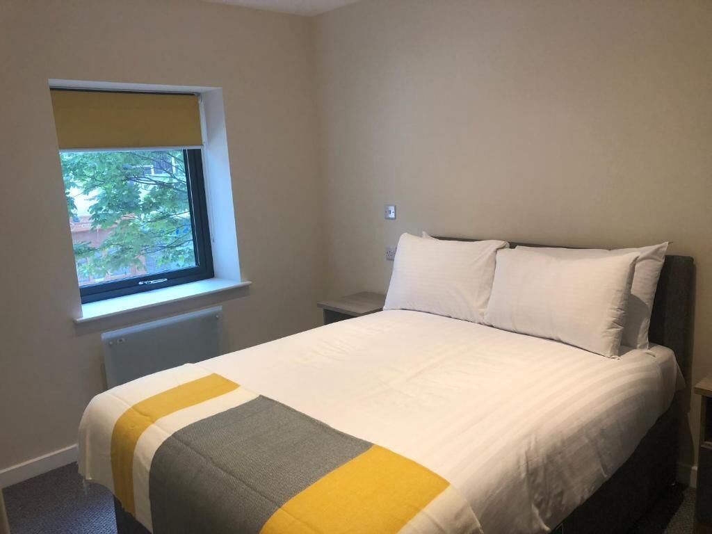 A bedroom with a bed, a window with a view, and a bedside table.