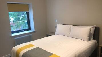 A bedroom with a bed, a window with a view, and a bedside table.