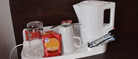 Una estación de café con una cafetera, un tarro de cristal, un paquete de galletas digestivas y un paquete de bolsitas de té.