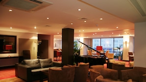 Um hall amplo com um piano de cauda, assentos confortáveis e grandes janelas com vista.