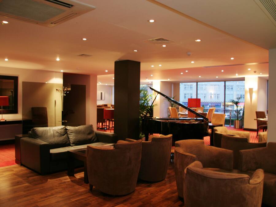 A spacious lobby with a grand piano, comfortable seating, and large windows offering a view.