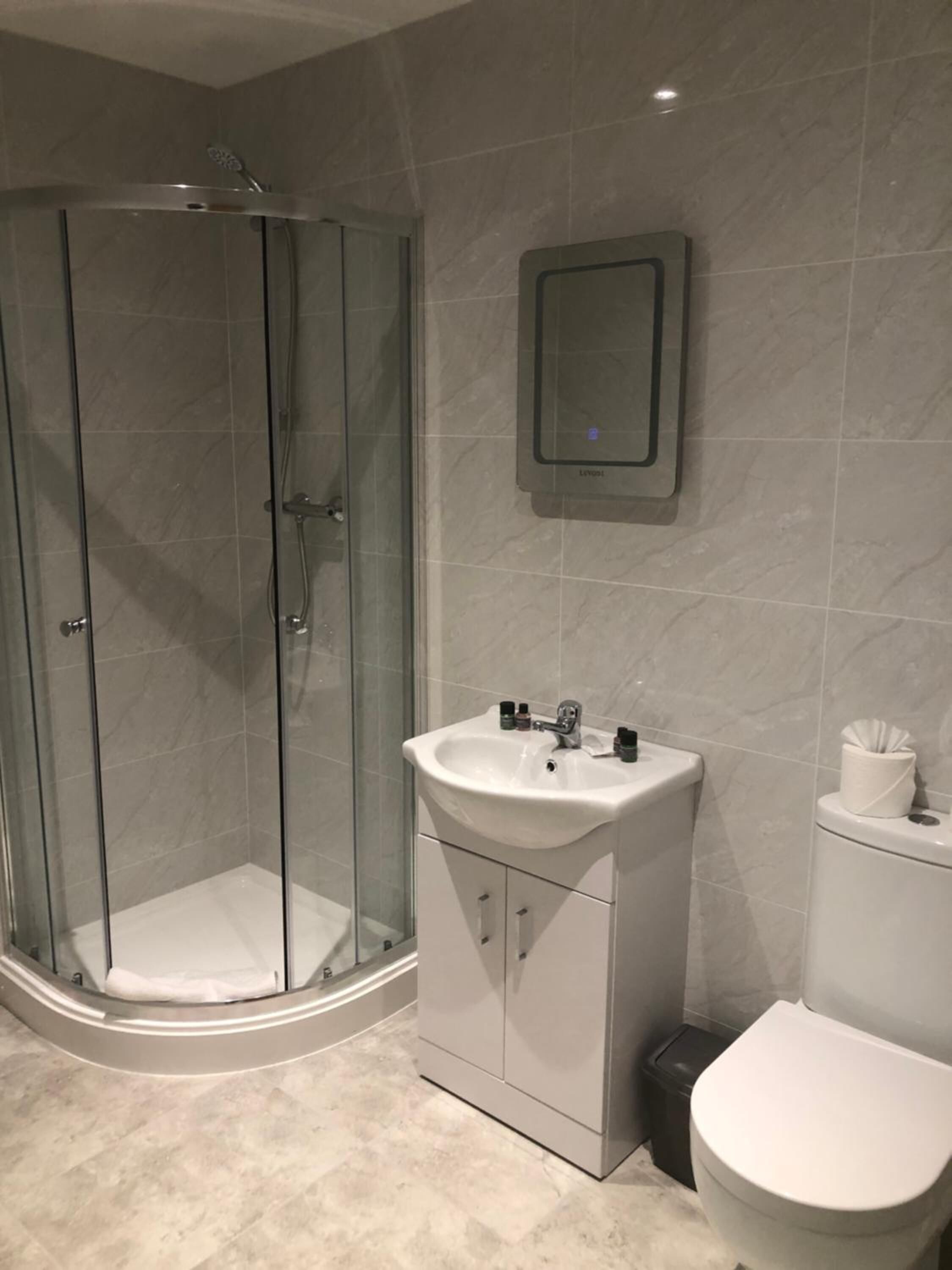 A modern bathroom with a glass-enclosed shower, a white sink with a mirror above it, and a toilet.