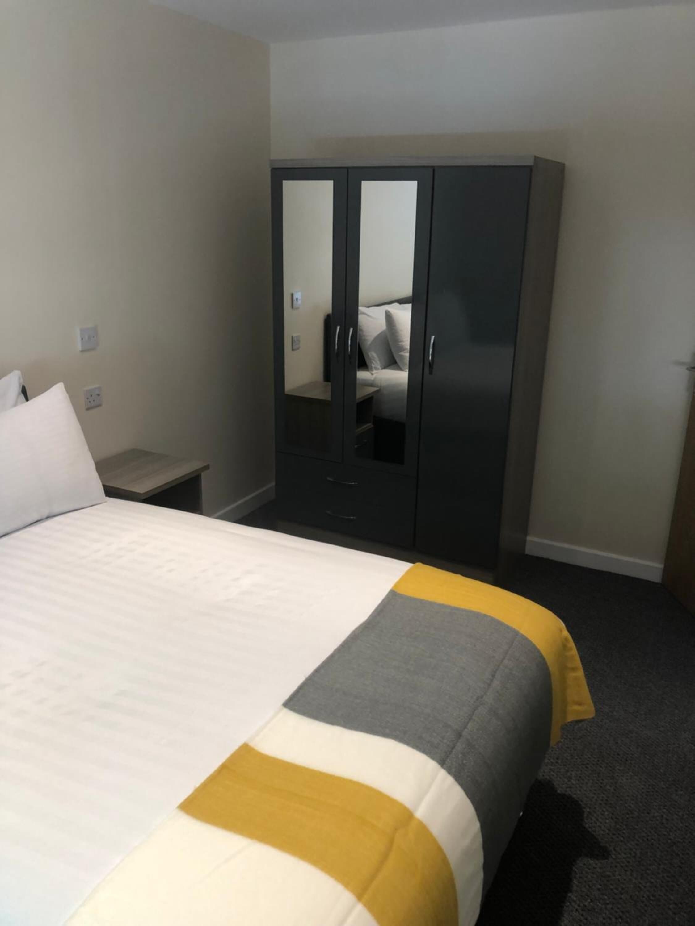 A hotel room with a bed, a wardrobe, and a nightstand.