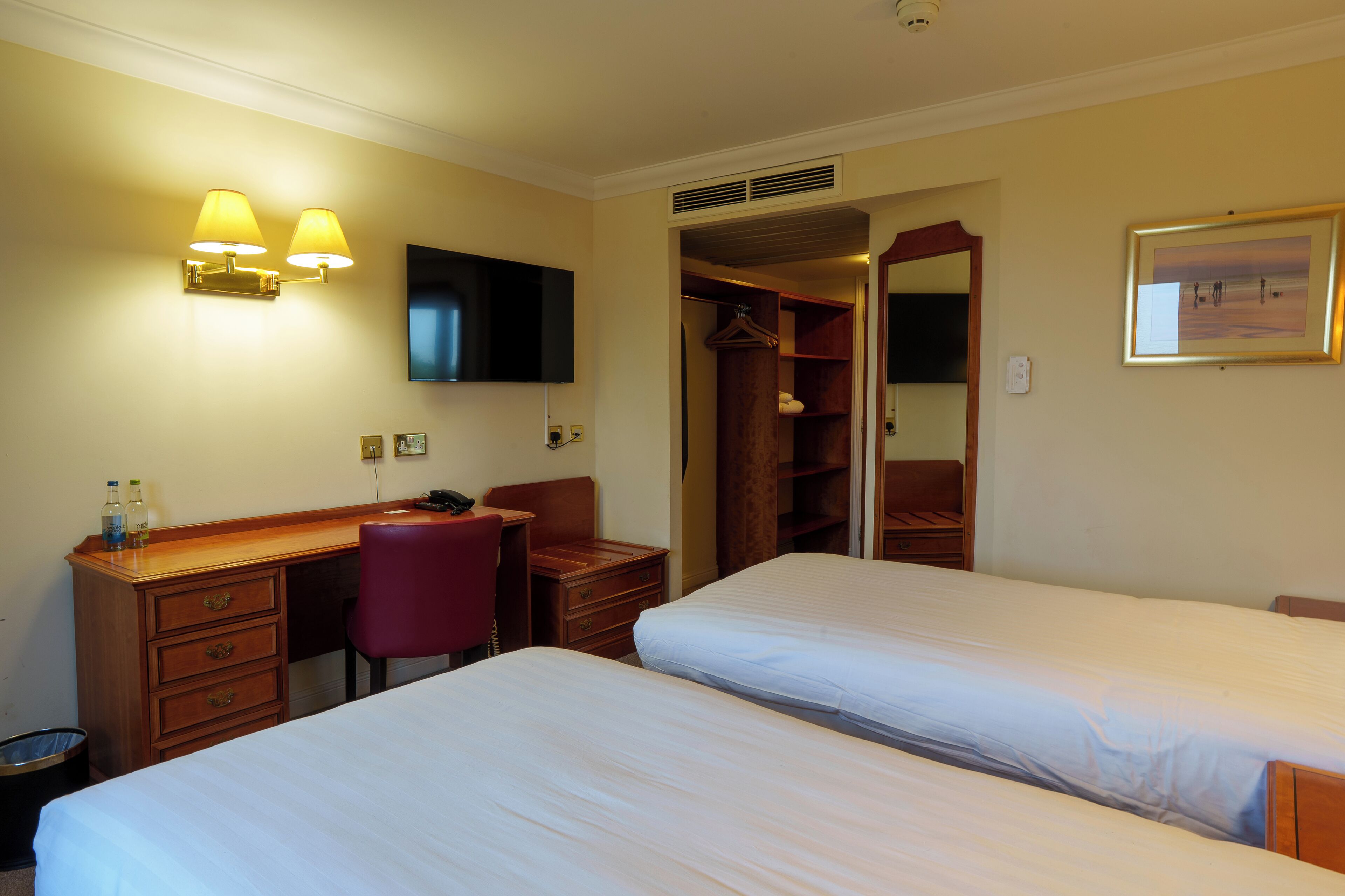 A hotel room with two beds, a desk, a chair, a TV, and a wardrobe.