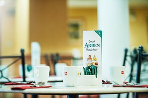 A breakfast setting with a menu titled "Great Arden Breakfast" on a table, accompanied by white cups and a coffee pot.
