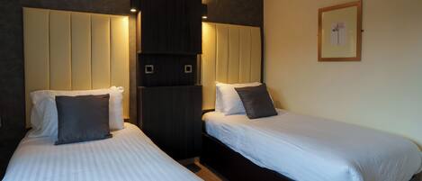 Two single beds with headboards, a dark wooden wardrobe, and a framed picture on the wall.