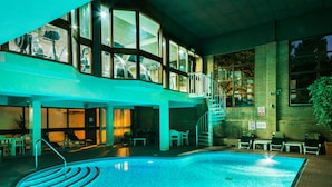 An indoor swimming pool with a clear pool edge, a staircase leading to an upper level, and a seating area with chairs and tables. - The Arden Hotel & Leisure Club (Solihull)