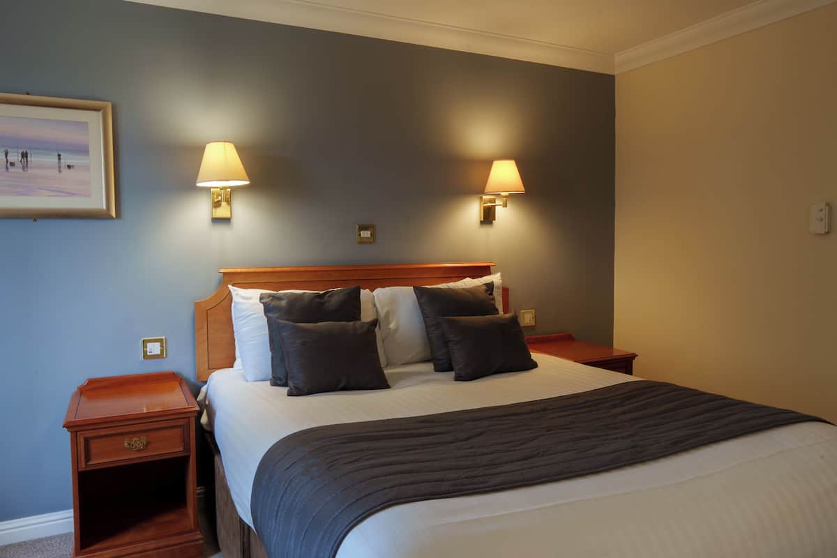 A neatly made bed with a dark blanket, two bedside lamps, and a framed picture on the wall.