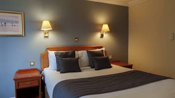Un lit bien fait, recouvert d’une couverture foncée, avec deux lampes de chevet et un tableau encadré accroché au mur.