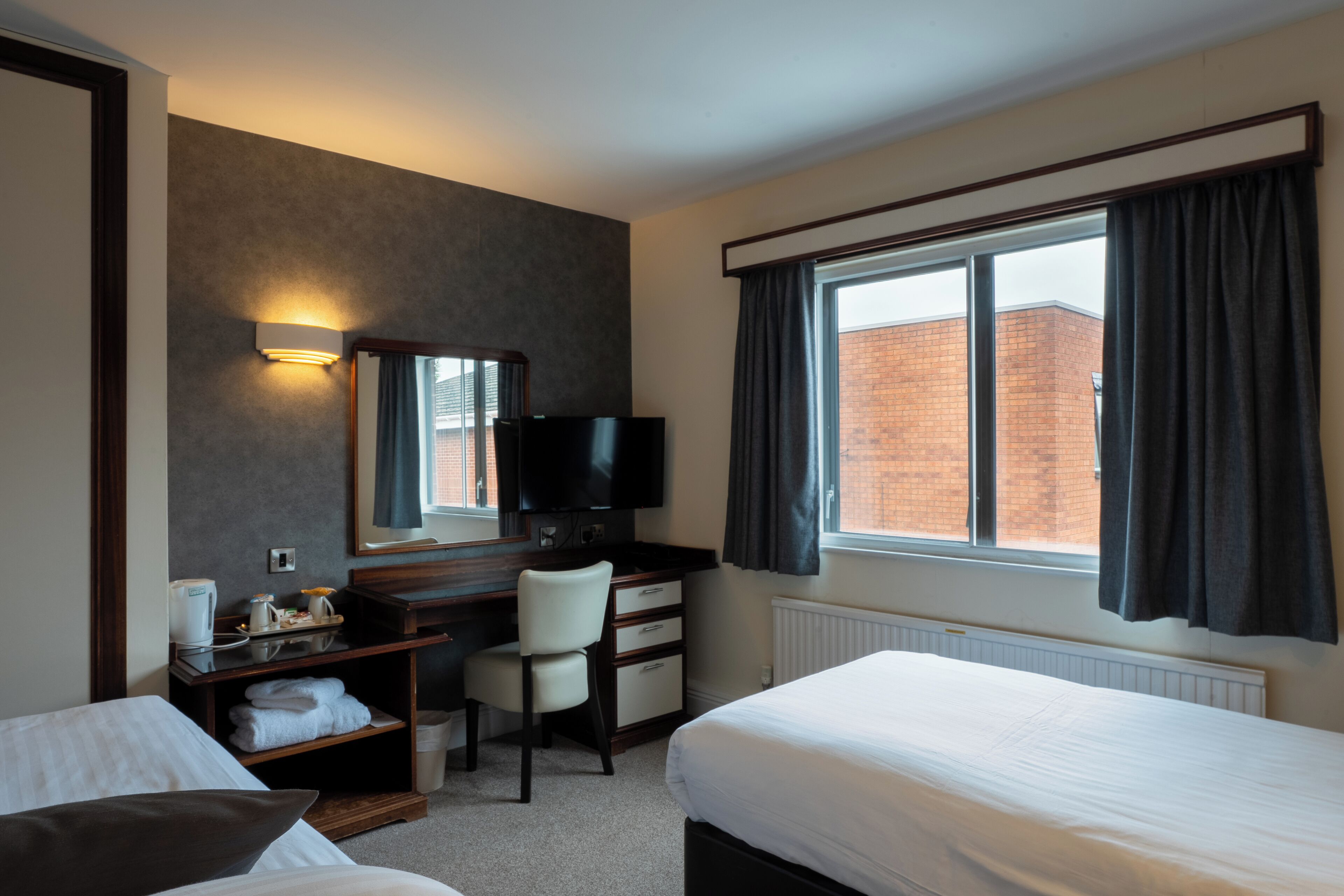A hotel room with a bed, a desk with a chair, a television, and a window with curtains.