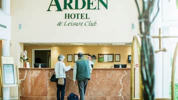 A reception desk at The Arden Hotel & Leisure Club with a marble counter and framed pictures above it.