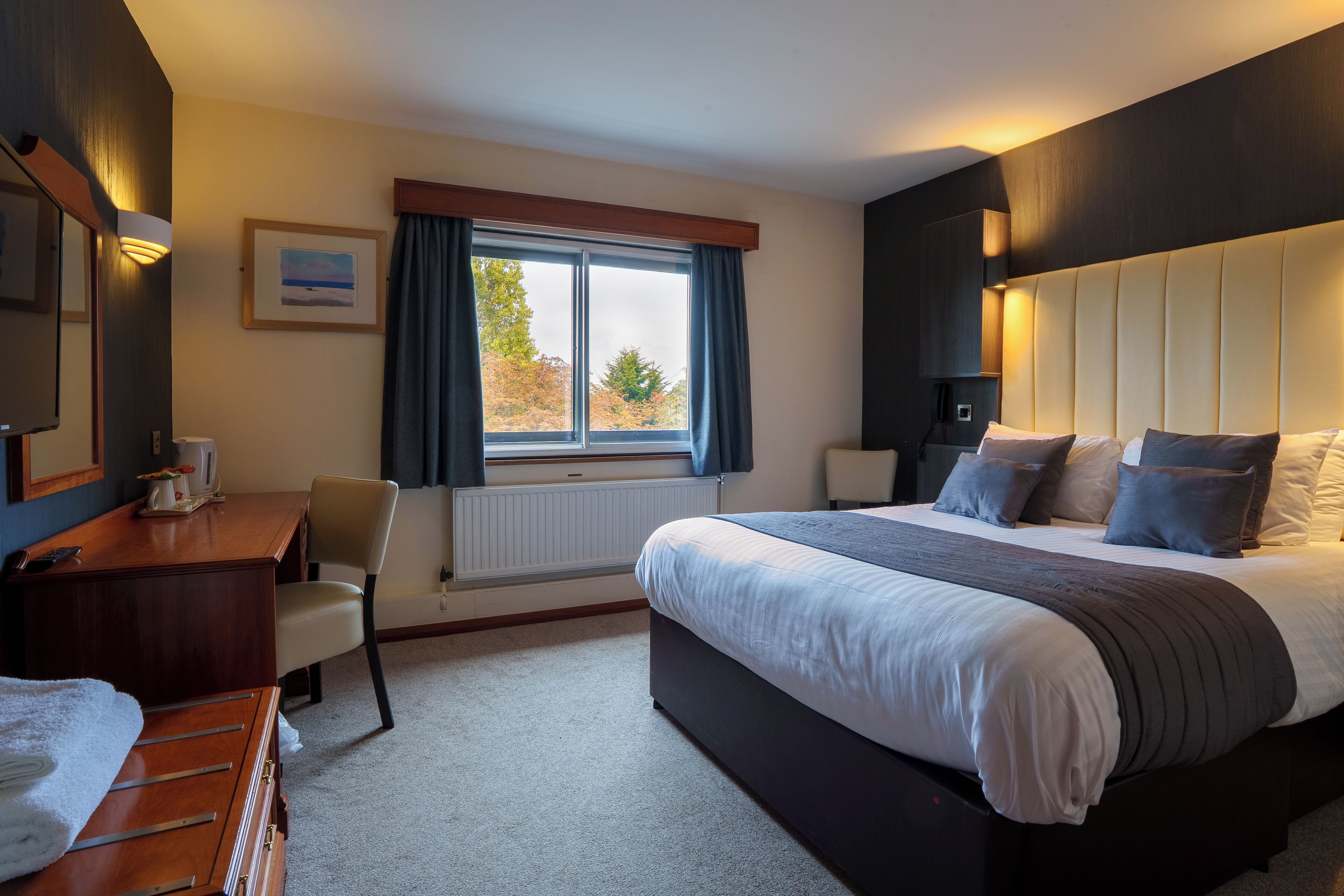 A modern hotel room with a large bed, a desk, and a chair.