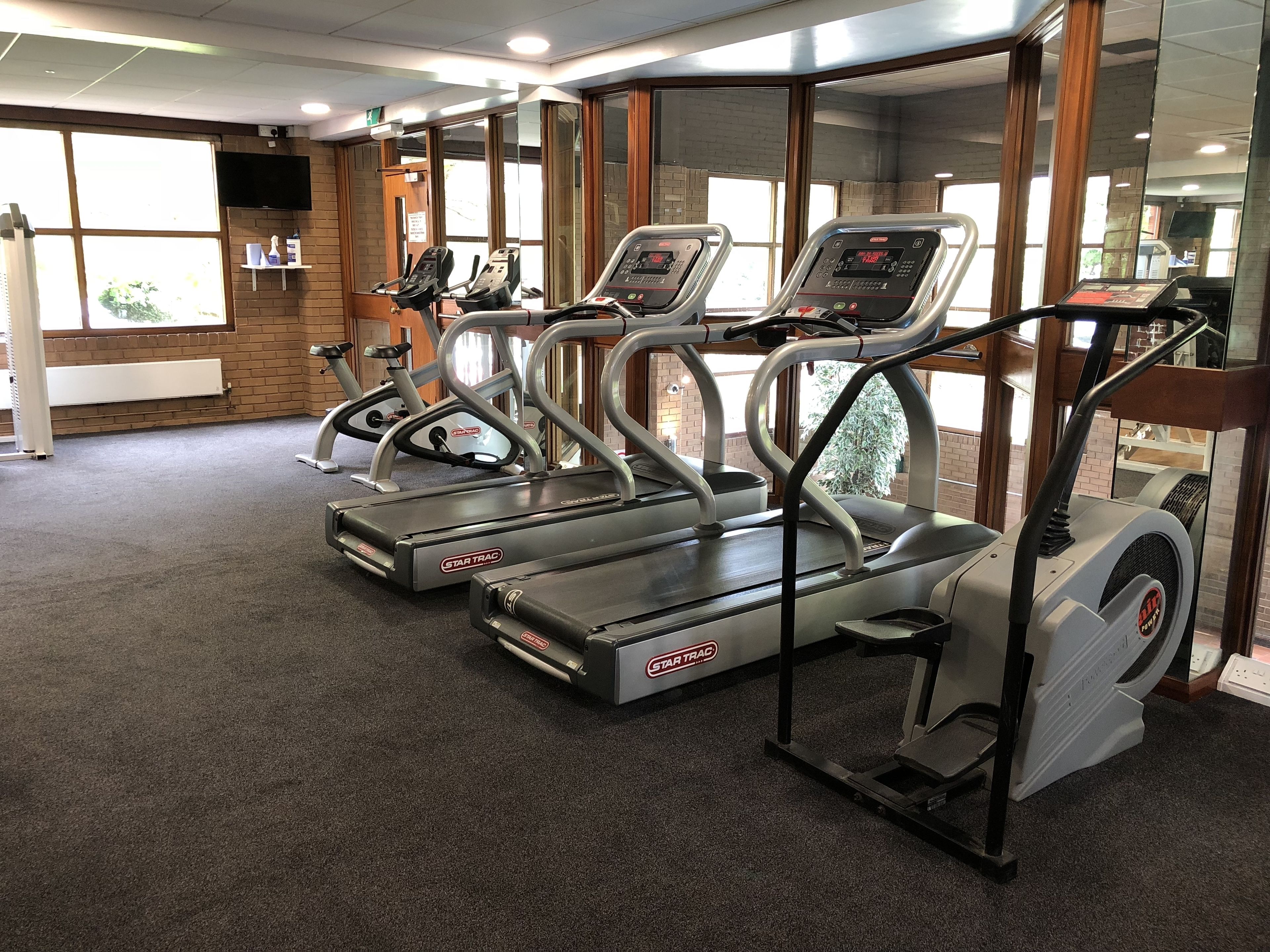 Un gimnasio con cintas de correr, bicicletas estáticas y un espejo grande.