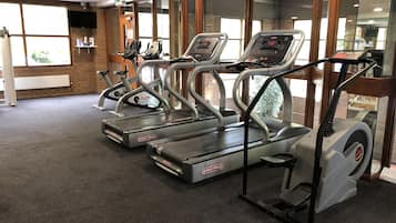 Un gimnasio con cintas de correr, bicicletas estáticas y un espejo grande.