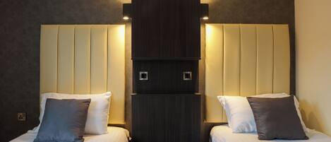 A hotel room with two beds, each with a pillow, a dark wood headboard, and a light-colored wall.