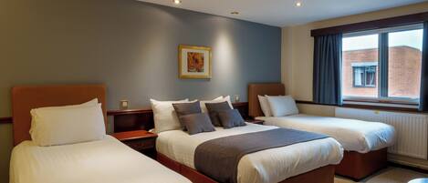 A hotel room with two single beds, a large window with curtains, a painting on the wall, and a radiator under the window.