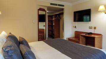 Una habitación de hotel con cama, escritorio, televisión, armario y espejo.
