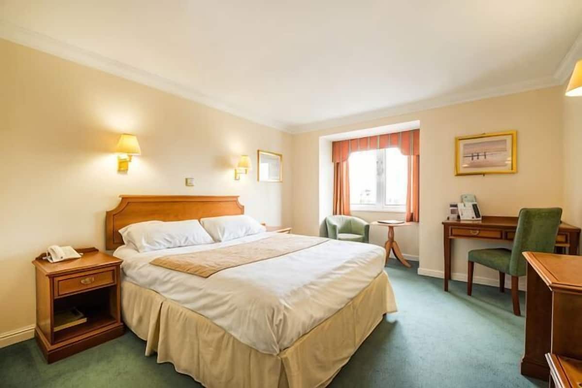Ein Hotelzimmer mit Bett, Nachttisch, Schreibtisch, Stuhl und einem Fenster mit Vorhängen.