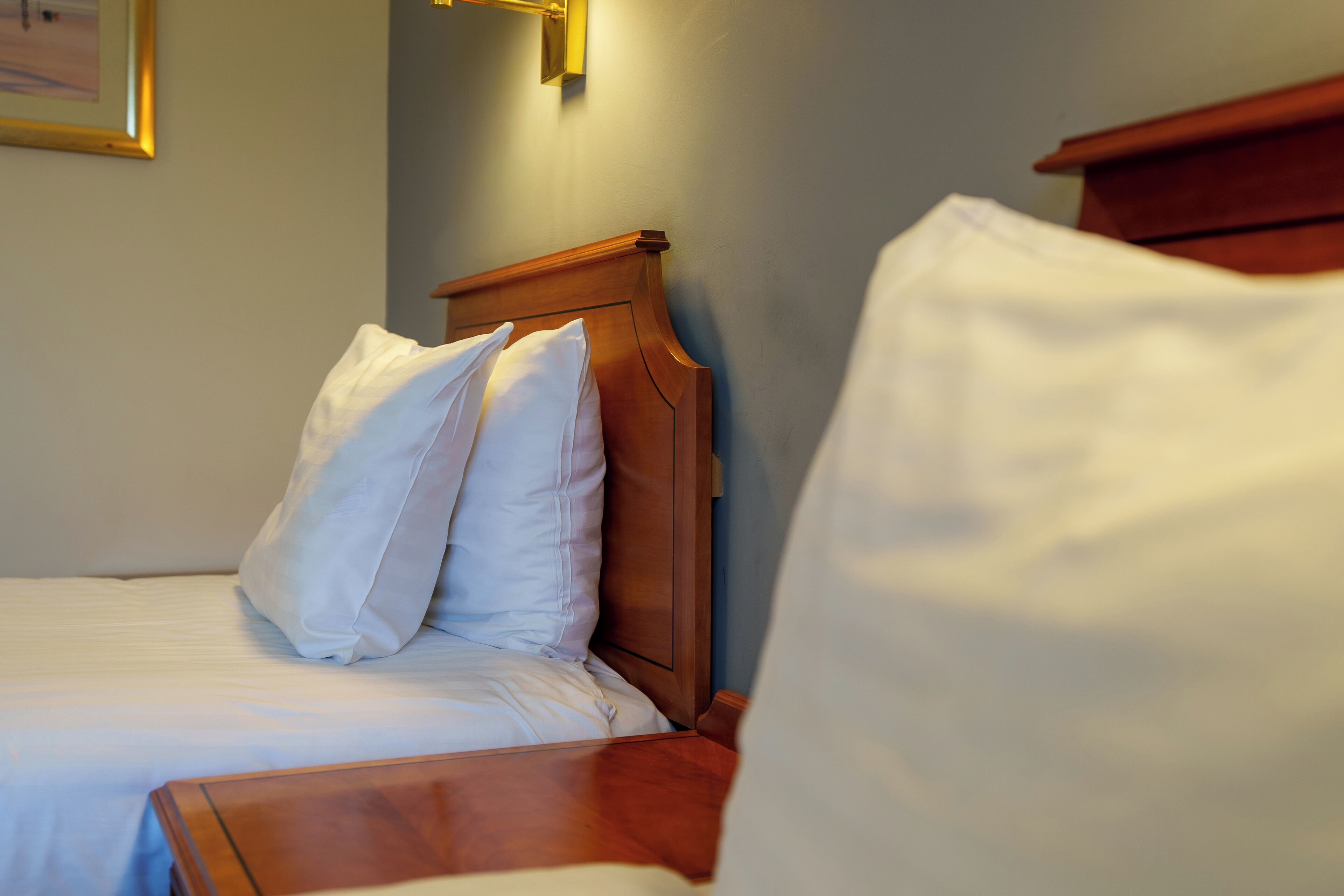 A neatly made bed with white linens and a wooden headboard.