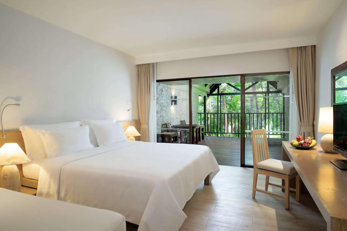A hotel room with a large bed, a desk with a chair, a TV, and a balcony with a table and chairs.