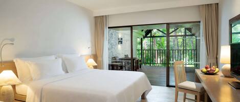 A hotel room with a large bed, a desk with a chair, a TV, and a balcony with a table and chairs.