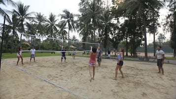 Partido de voleibol en una cancha de arena rodeada de palmeras.