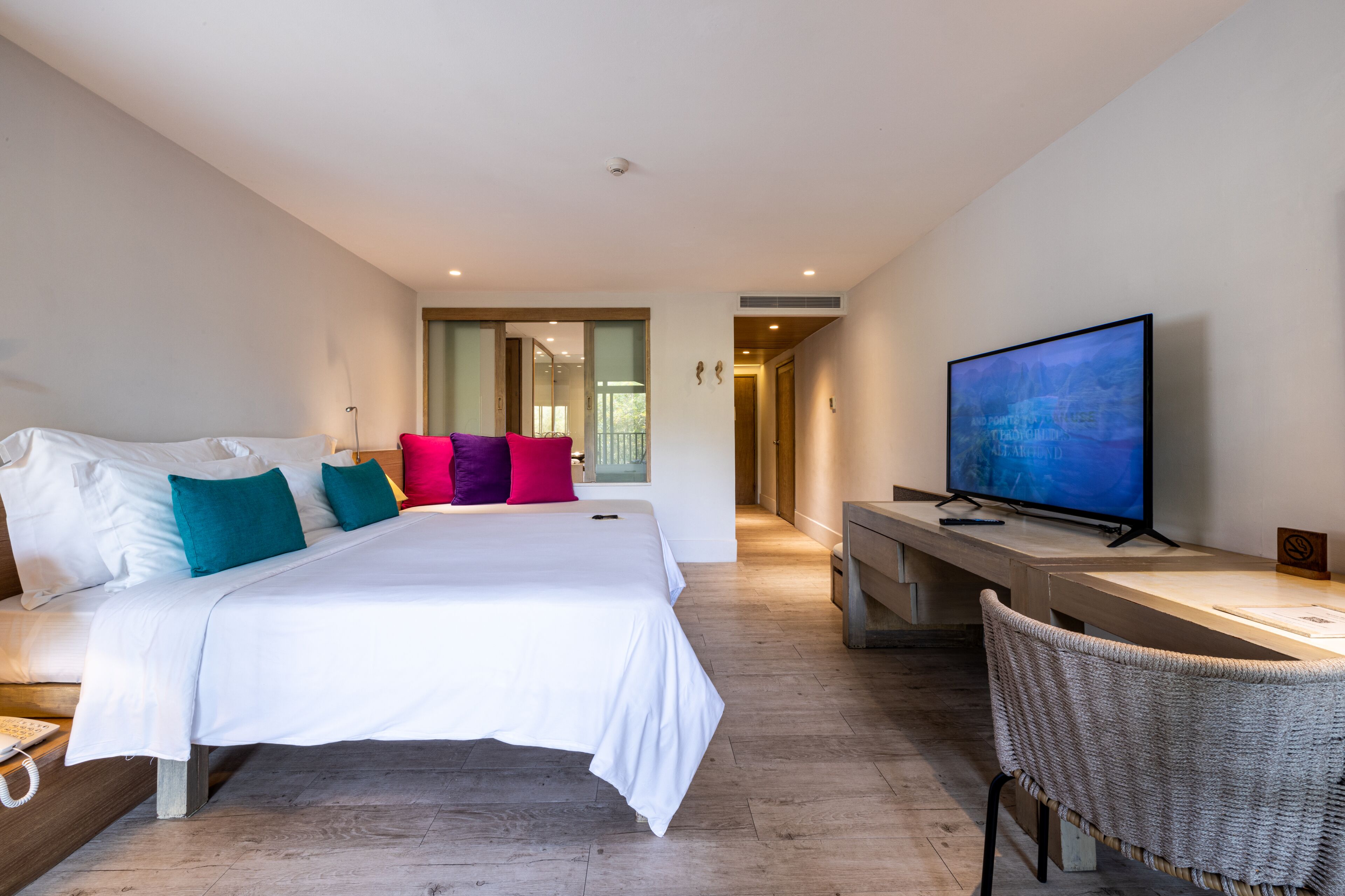 Een moderne hotelkamer met een groot bed, een bureau met een televisie en uitzicht op de gang.