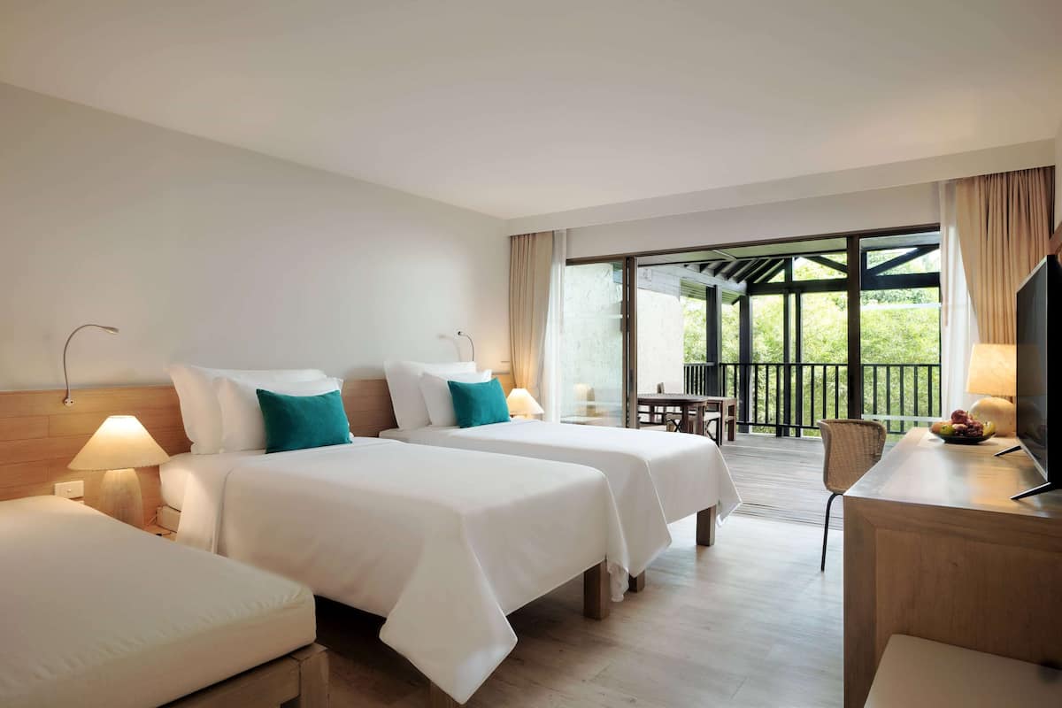 A hotel room with two beds, a desk, a chair, and a TV.
