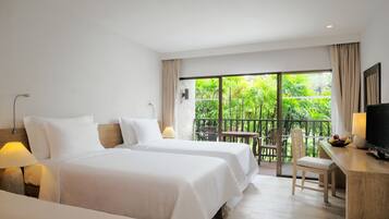 A hotel room with two beds, a desk with a chair, a TV, and a balcony with a table and chairs.