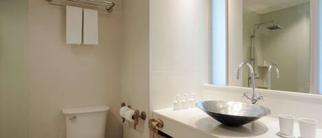 Un baño moderno con inodoro blanco, cabina de ducha de vidrio, un espejo grande y un lavabo blanco con cuenca.