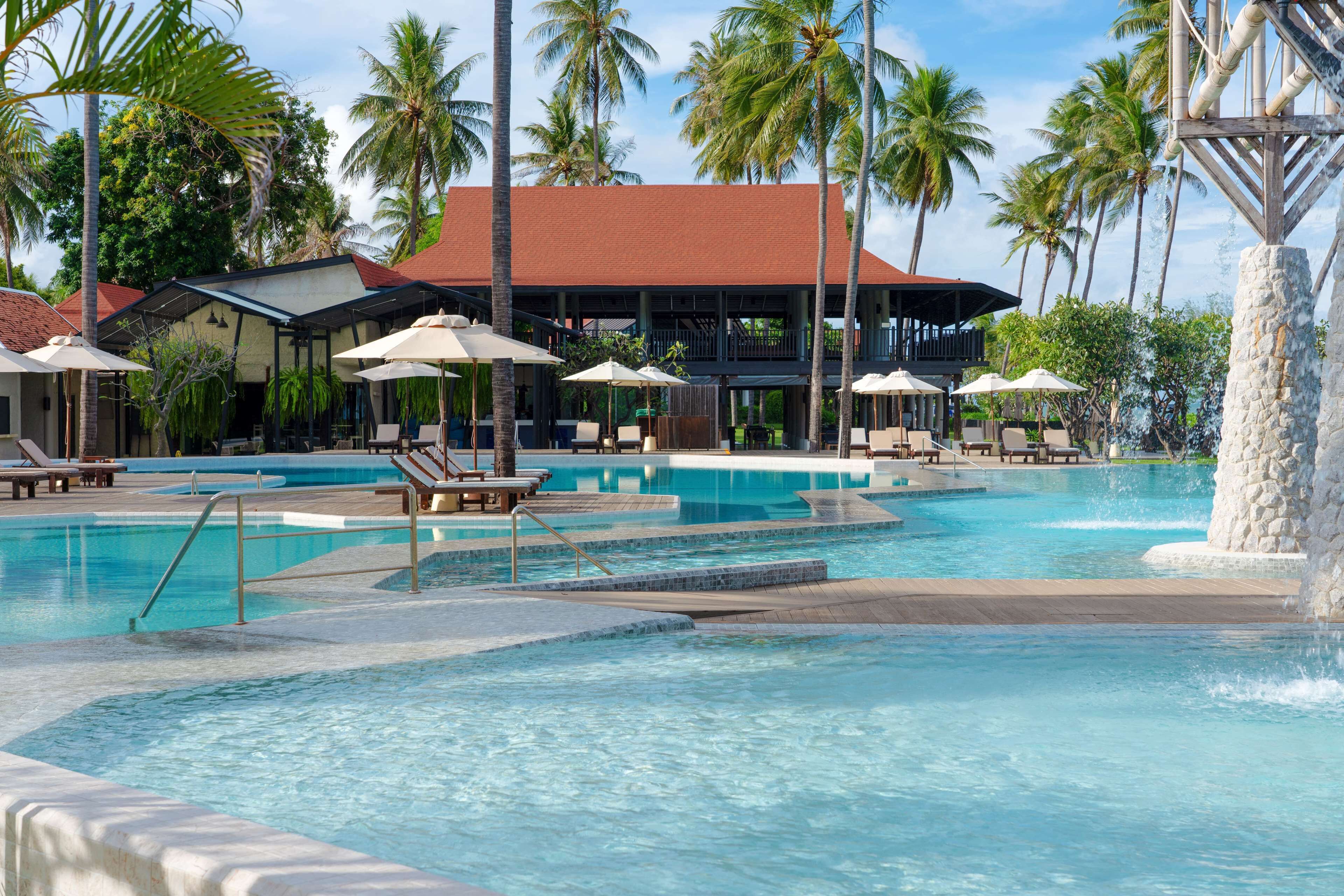 A pool area with multiple levels, lounge chairs, umbrellas, and palm trees.
