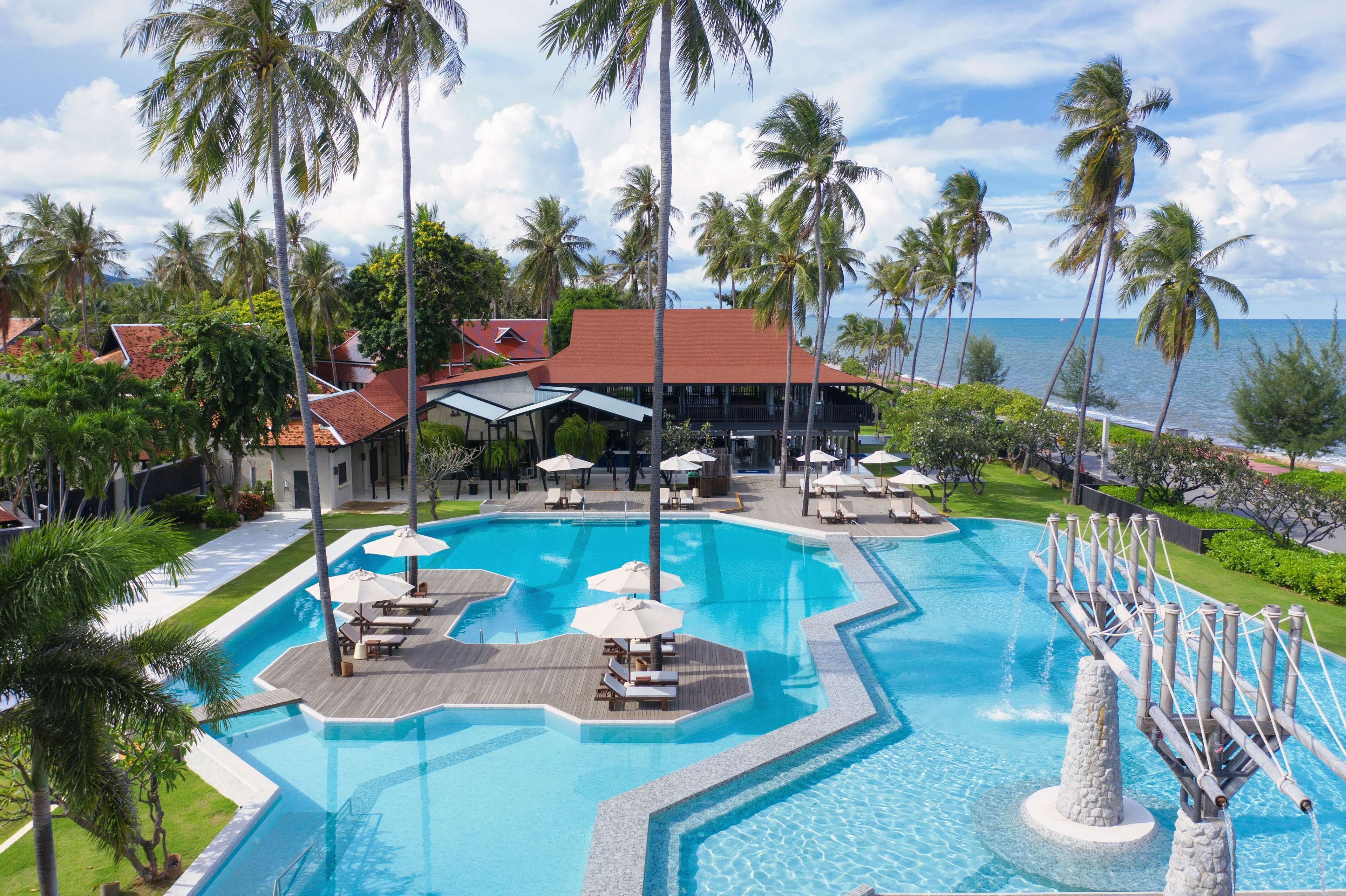 Un resort con una grande piscina, palme e vista sull'oceano.