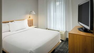 Ein Hotelzimmer mit Bett, Fernseher auf einem Holzboden, einer Lampe und einem fenster mit Vorhängen.