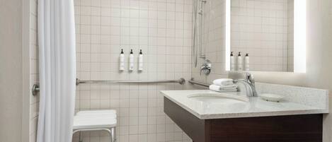 A modern bathroom with a shower, a sink, and a mirror. There are toiletries on the wall and a towel rack.