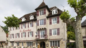 Een traditioneel Europees gebouw met een bord waarop 'Le Beauclieu' staat. Het heeft een stenen gevel, meerdere ramen met luiken en een balkon met terrasstoelen.
