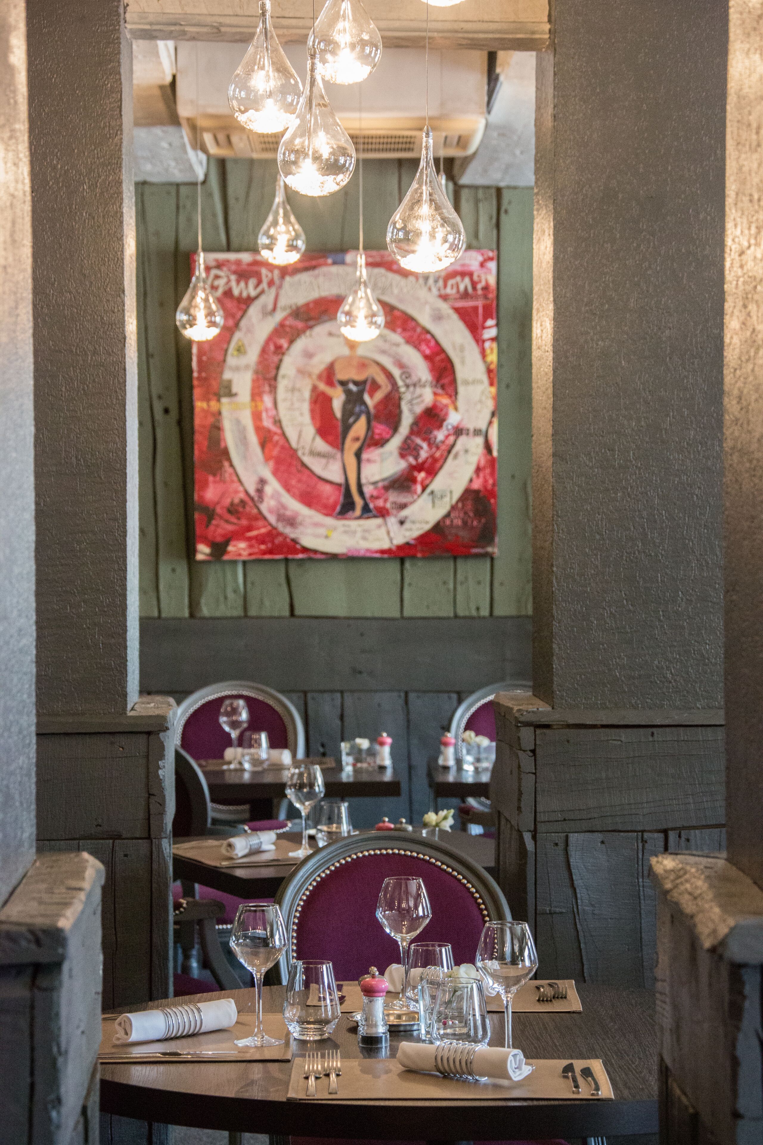 Interno di un ristorante con tavoli di legno, lampade a sospensione e un'ampia pittura astratta appesa al muro.