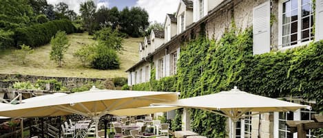 An outdoor café with tables and chairs, surrounded by a stone wall and greenery.