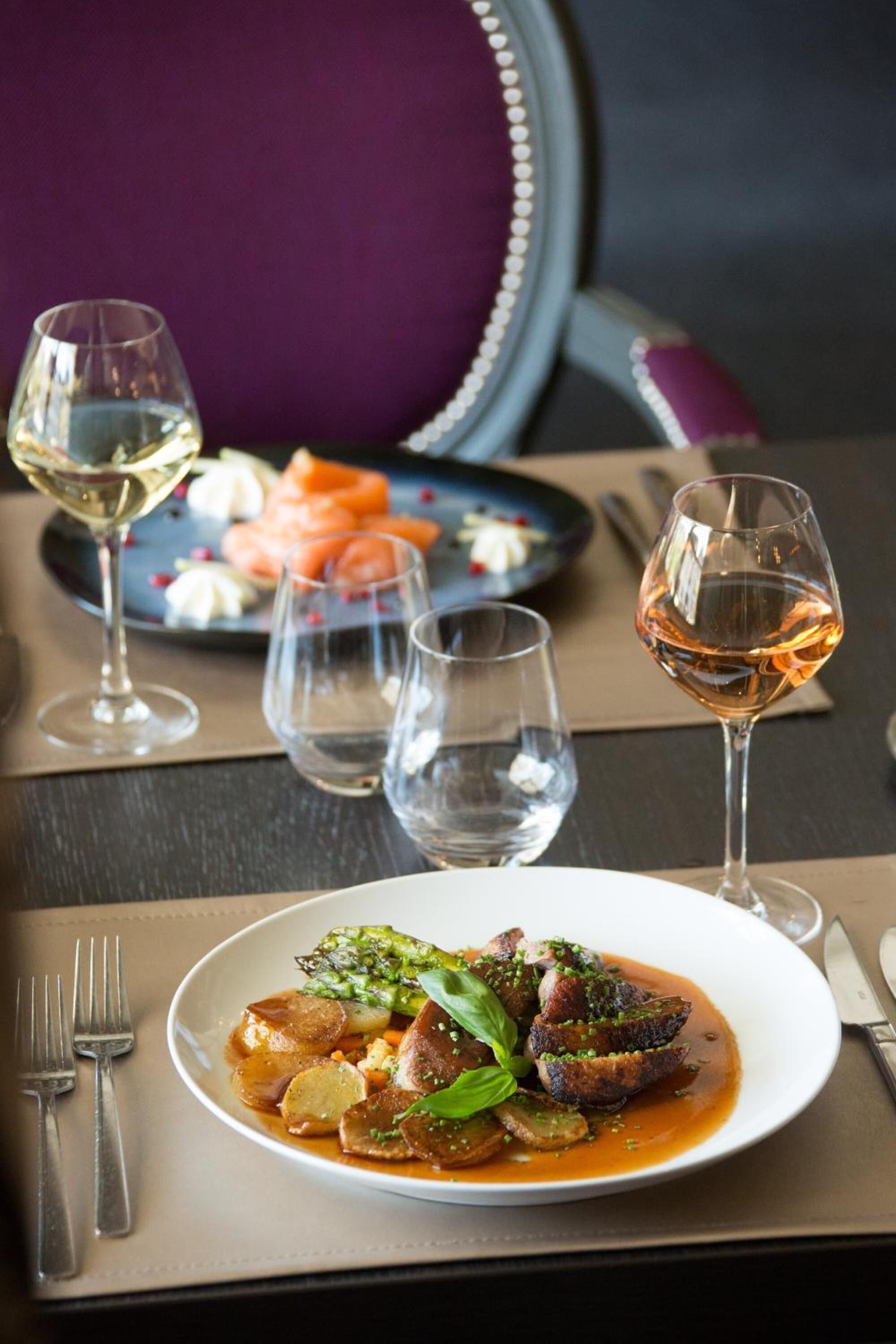 A dining table with a plate of food, two glasses of wine, and a fork.