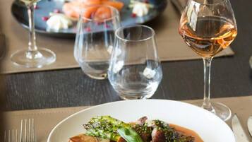 A dining table with a plate of food, two glasses of wine, and a fork.
