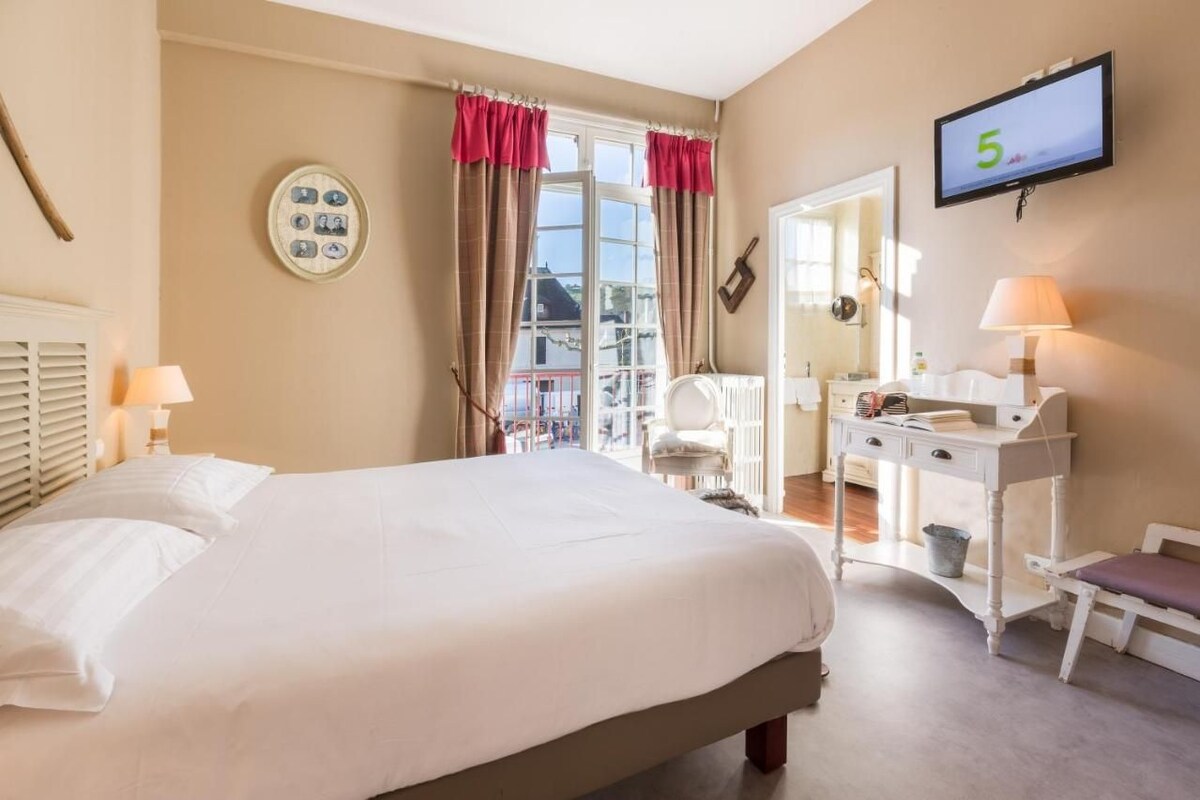 Ein Hotelzimmer mit Bett, Schreibtisch, Stuhl, Fernseher und einem Fenster mit Vorhängen.