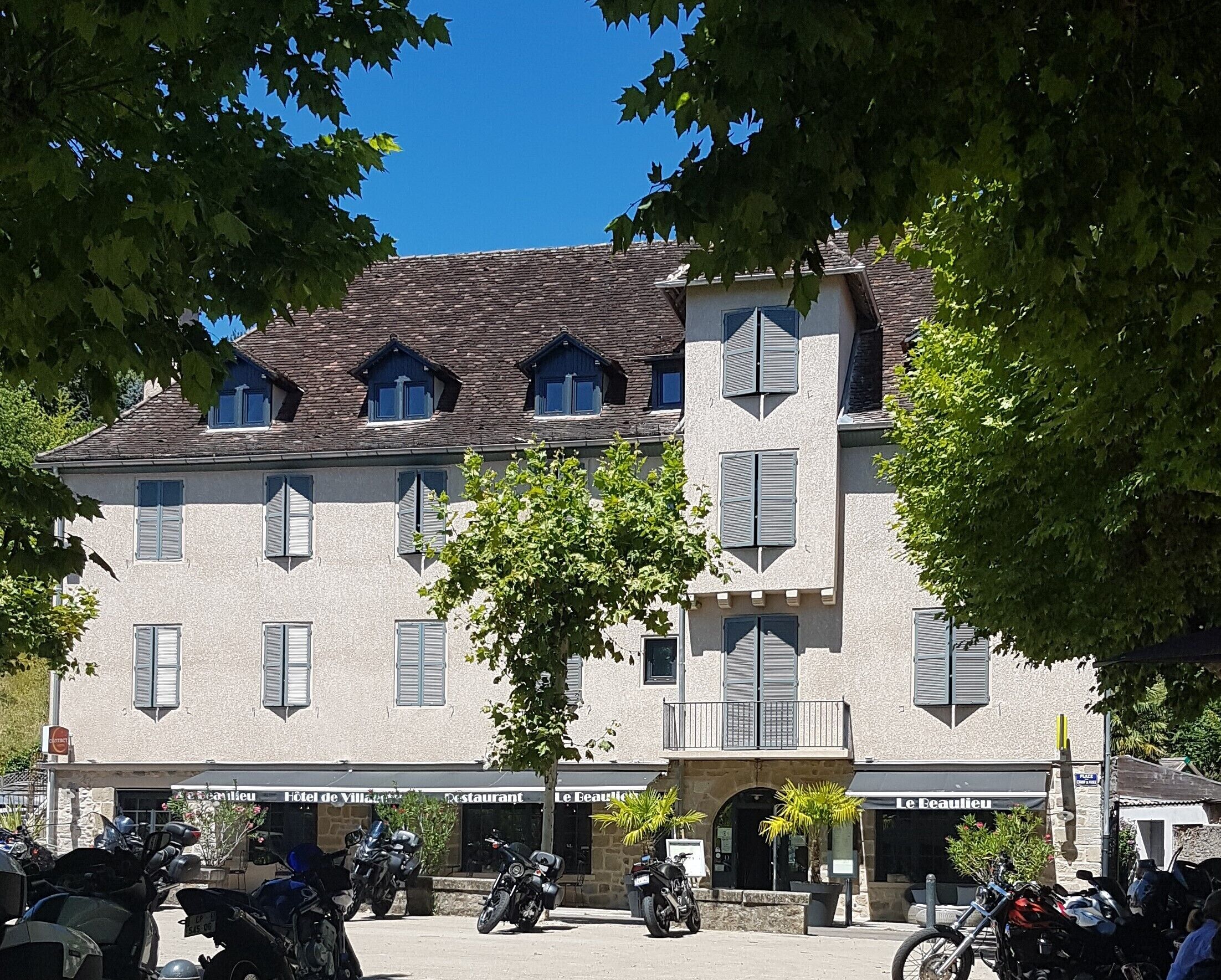 A building with multiple windows and shutters, a sign for a restaurant, and several parked motorcycles.