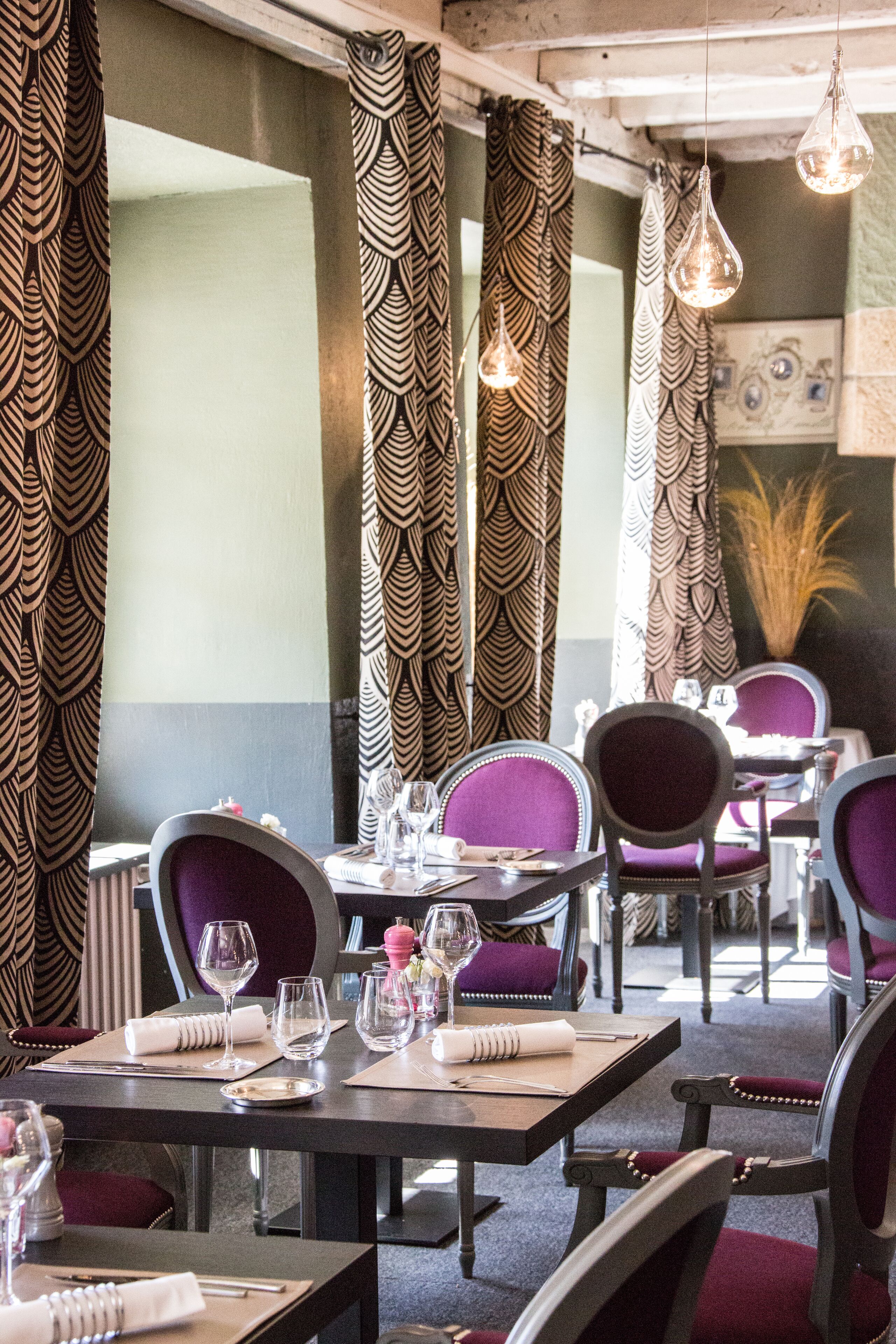 Een restaurantinterieur met behangpatronen, paarse beklede stoelen en hangende lampen.