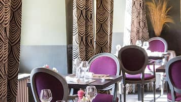 Een restaurantinterieur met behangpatronen, paarse beklede stoelen en hangende lampen.